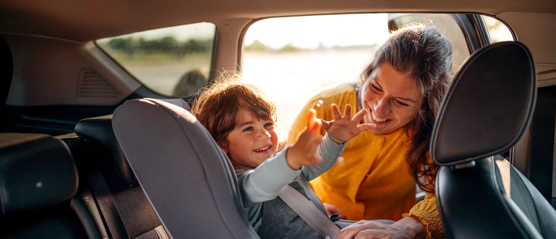 Strahlendes Kind sitzt im Kindersitz im Auto und wird von seiner Mutter angeschnallt 