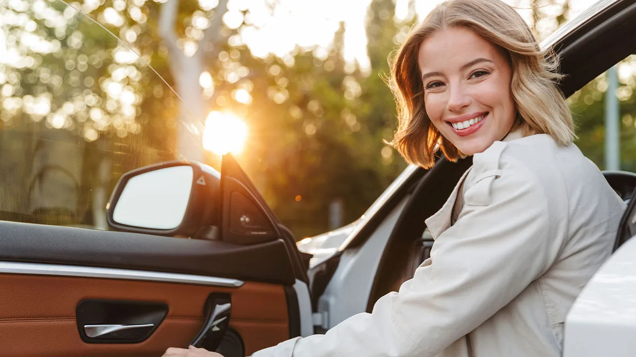 Lächelnde Frau steigt gerade in ihr Auto ein 