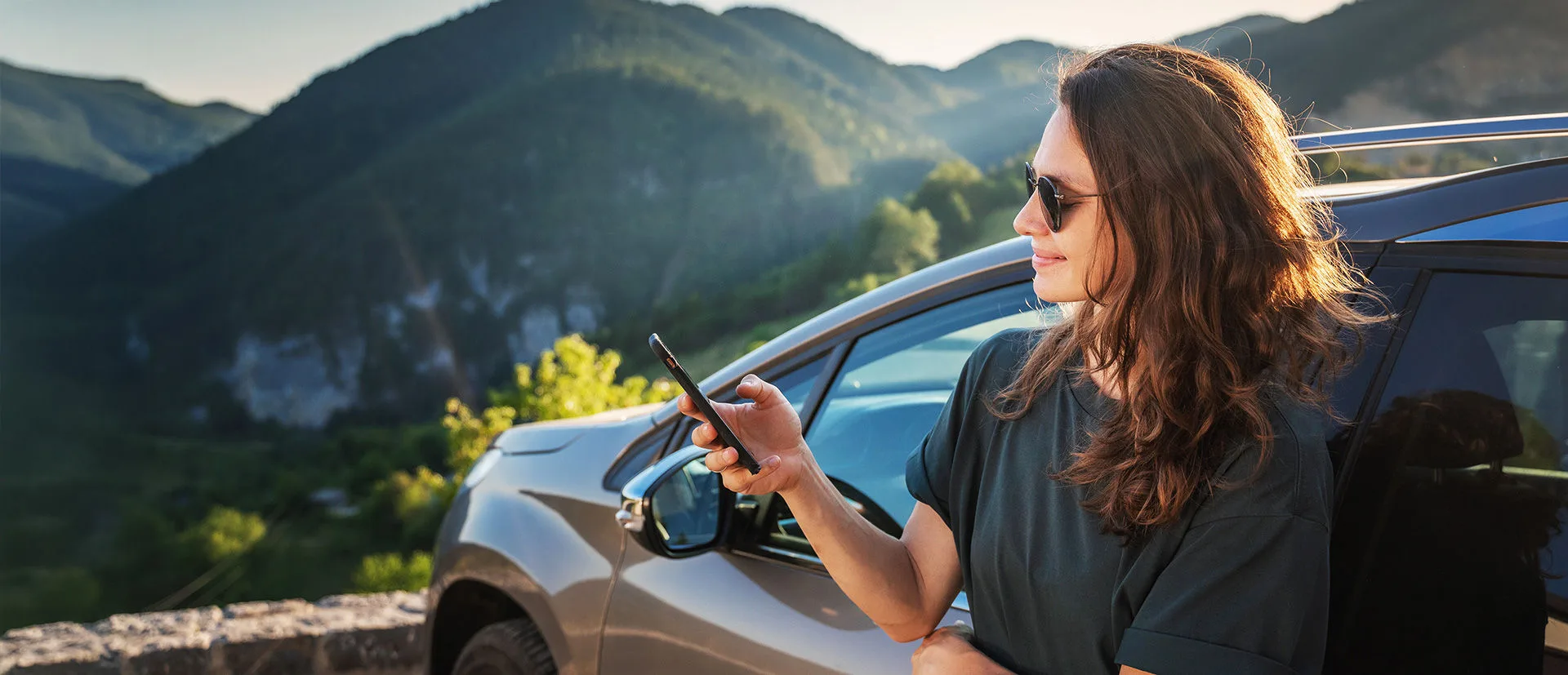 Frau mit Sonnenbrille lehnt am ato und schaut zufrieden in ihr Handy